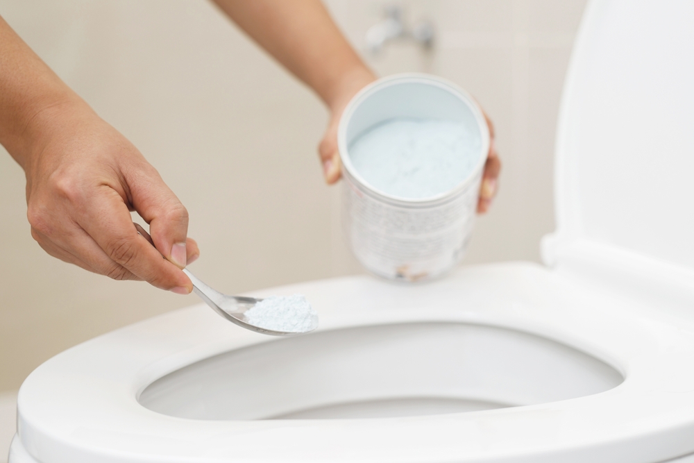 ผู้หญิงกำลังเทสารฟอกขาวในโถส้วมเพื่อกำจัดกลิ่นอับในห้องน้ำ